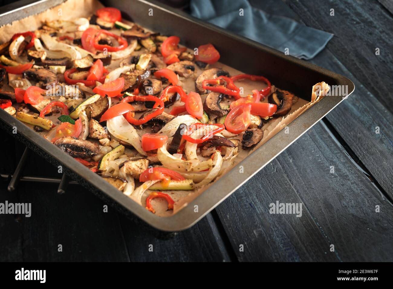 Gesundes Ofengemüse wie Paprika, Tomaten, Zucchini, Pilze, Fenchel und Auberginen auf einem Backblech auf dunklem rustikalem Holz, ausgewählter Fokus, nar Stockfoto