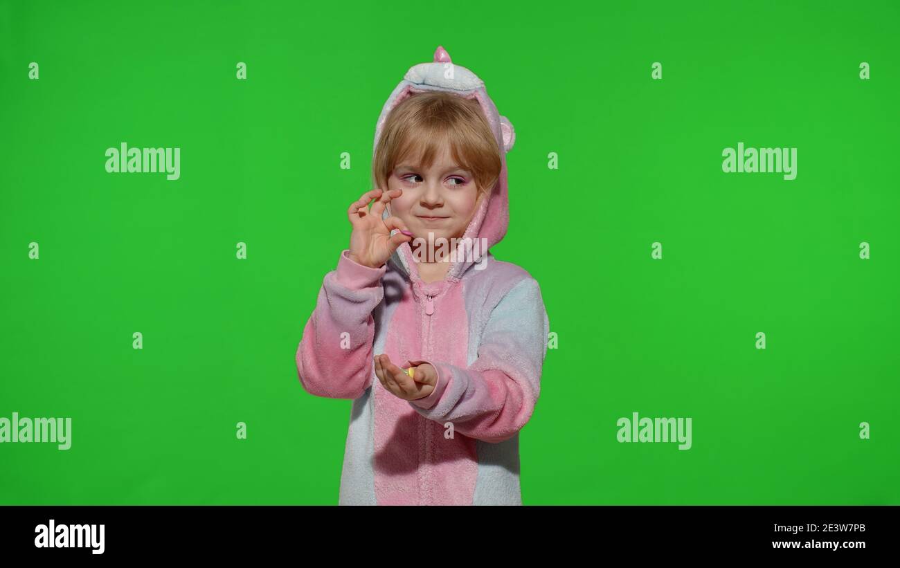 Portrait eines niedlichen kleinen Kindes lächelnd, genießen essen Süßigkeiten Süßigkeiten Dessert im Einhorn-Kostüm auf Chroma-Schlüssel grünen Hintergrund. Modell Kind Mädchen Animator in Einhorn Pyjamas. Speicherplatz kopieren Stockfoto