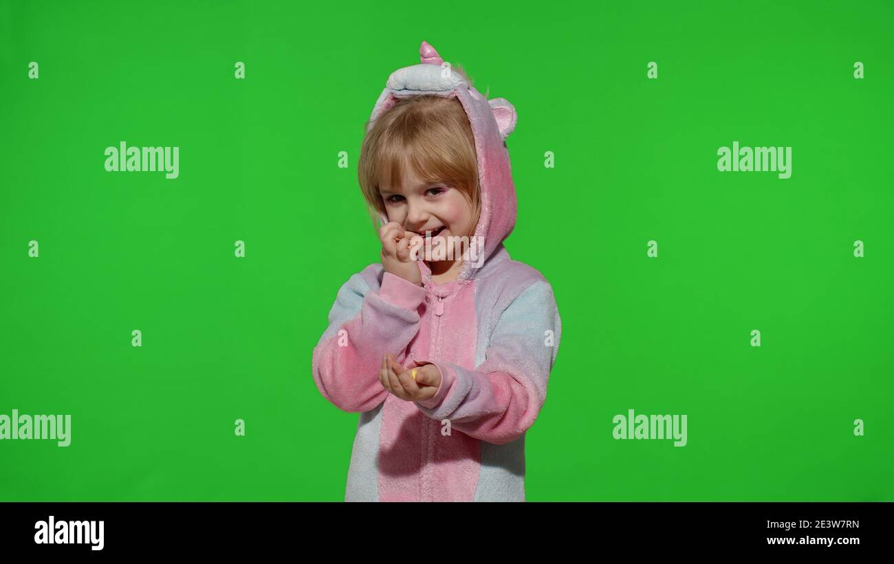 Portrait eines niedlichen kleinen Kindes lächelnd, genießen essen Süßigkeiten Süßigkeiten Dessert im Einhorn-Kostüm auf Chroma-Schlüssel grünen Hintergrund. Modell Kind Mädchen Animator in Einhorn Pyjamas. Speicherplatz kopieren Stockfoto
