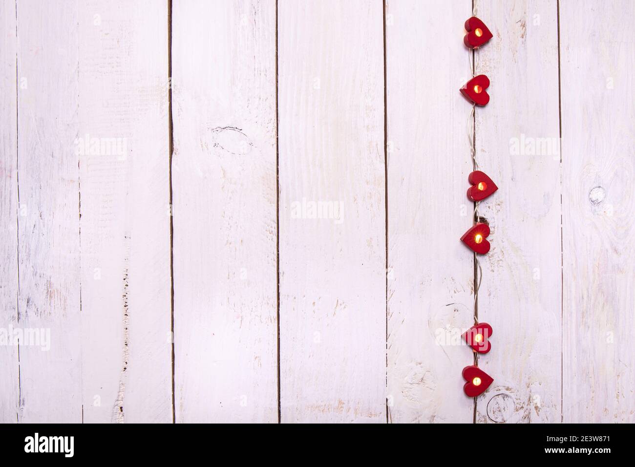 Eine Kette von kleinen Lichtern in roten Herzen auf einem weißen Holzhintergrund. Schäbiger Chic, rustikale und intime Atmosphäre. Stockfoto
