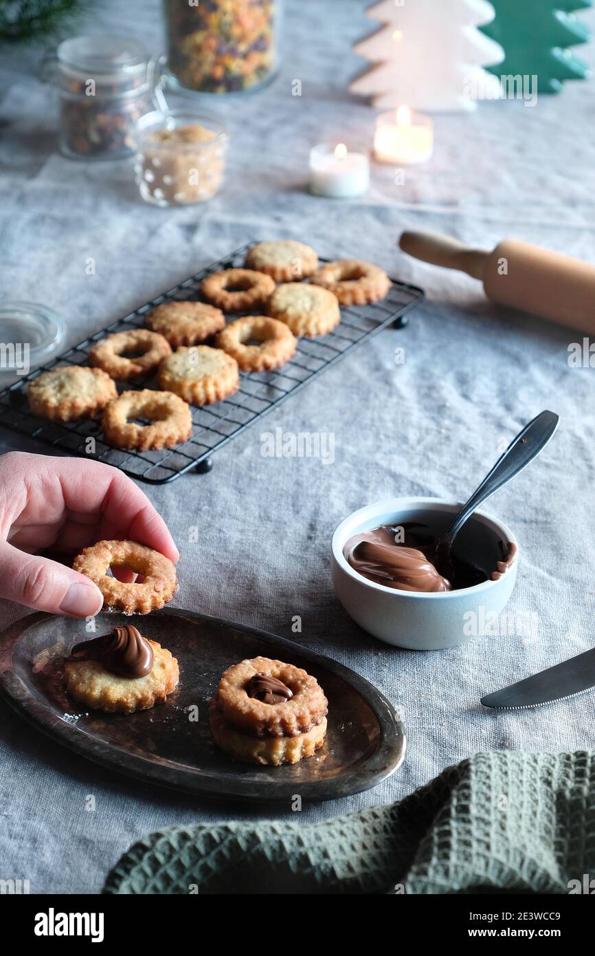 Sandwichkekse gefüllt mit Haselnussaufstrich, Nougatcreme. Weihnachtsbäume, Kerzen auf Leinentischdecke. Tageslicht. Stockfoto