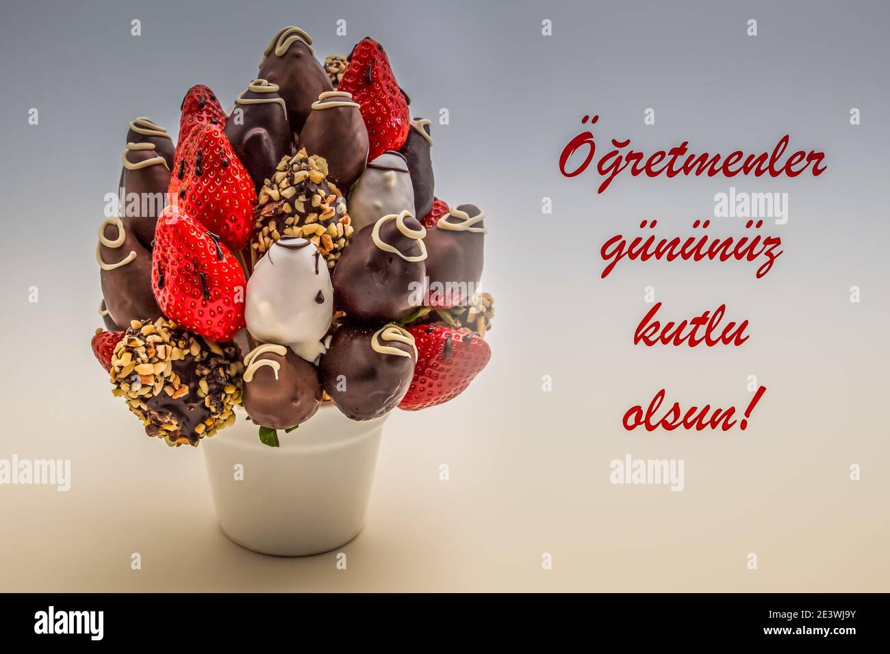 Happy Teacher's Day Grußkarte in türkischer Sprache mit rotem Schriftzug, der Ogretmenler gunuz kutlu olsun liest; Strauß essbarer Blumen, arrangem Stockfoto