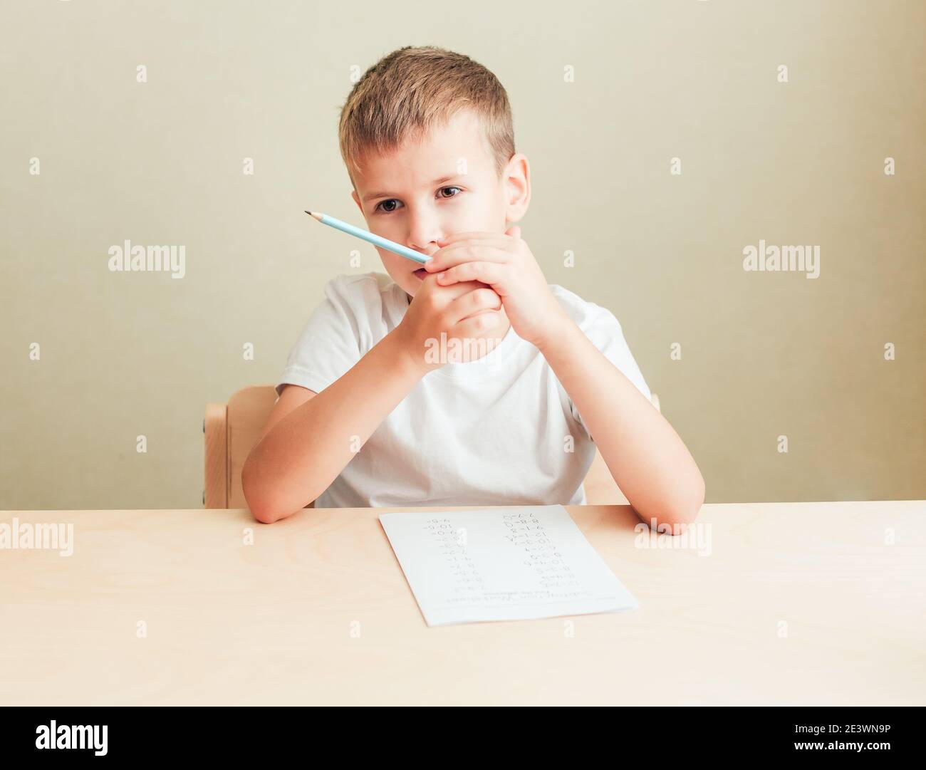 7 Jahre alter Junge, der mit Laken am Schreibtisch sitzt Von Papier und Bleistift und Mathematiktest Stockfoto