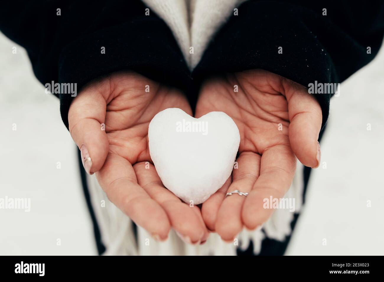 Schnee Herz Schneeball in Mädchen Handschuhen. Unscharfer Hintergrund Stockfoto
