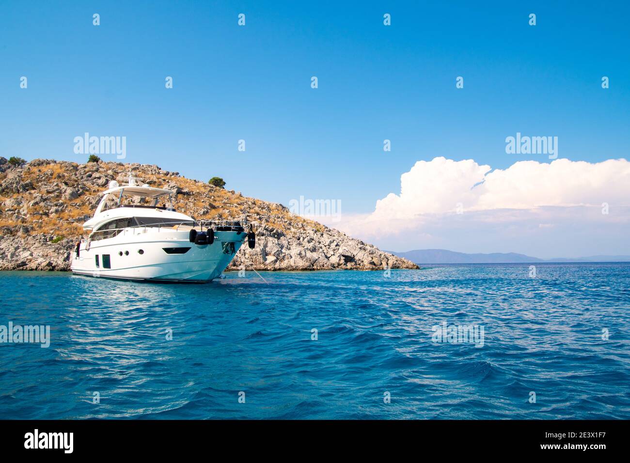 Ein weißes Luxus-Segelschiff in einer türkisfarbenen wunderschönen Meeresbucht verankert. Im Hintergrund felsige Insel und weiße Wolken mit Kopierraum Stockfoto