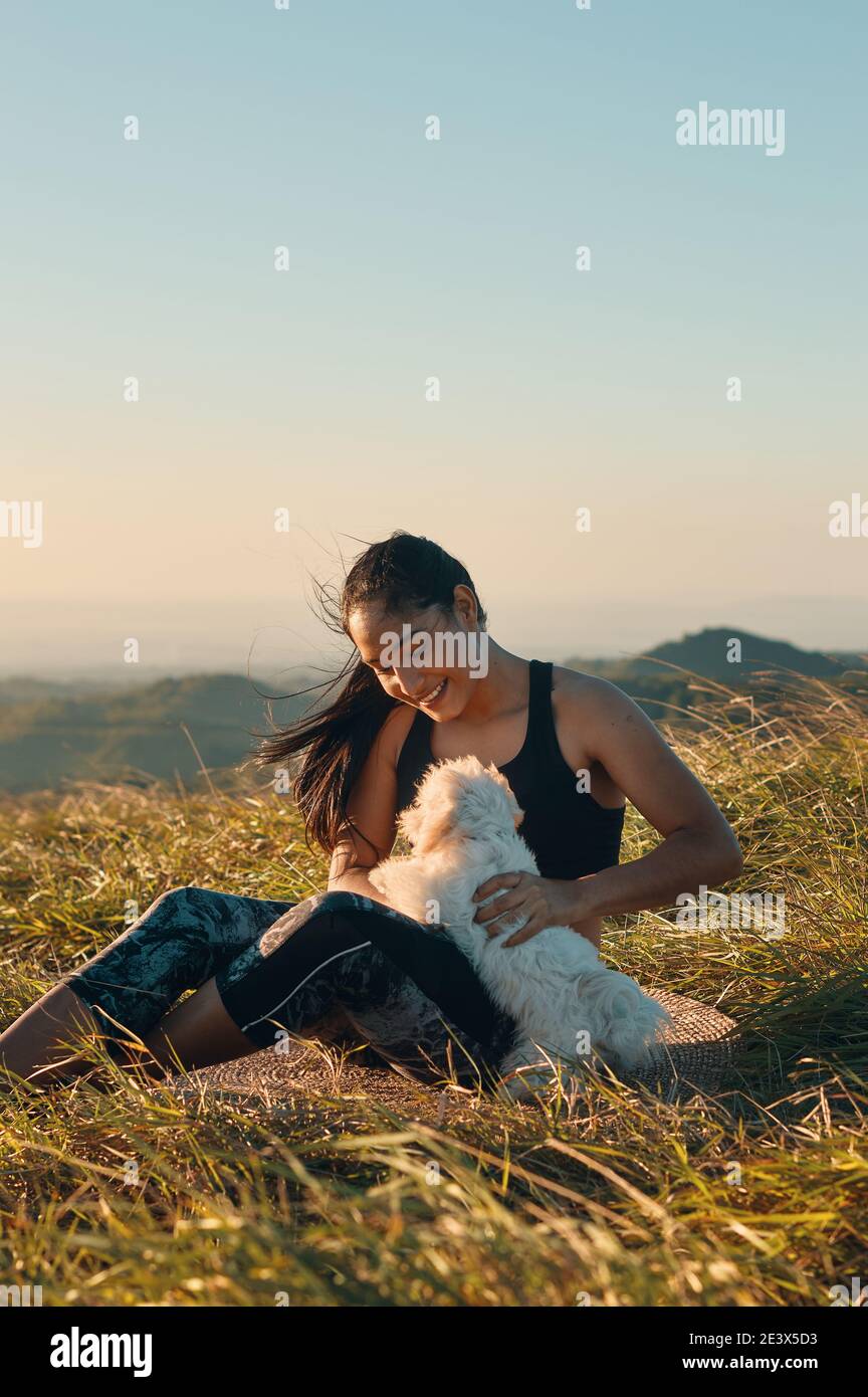 Eine glückliche junge Frau, die auf dem Gras sitzt und mit ihr spielt Ihr wunderschöner Welpenhund Stockfoto