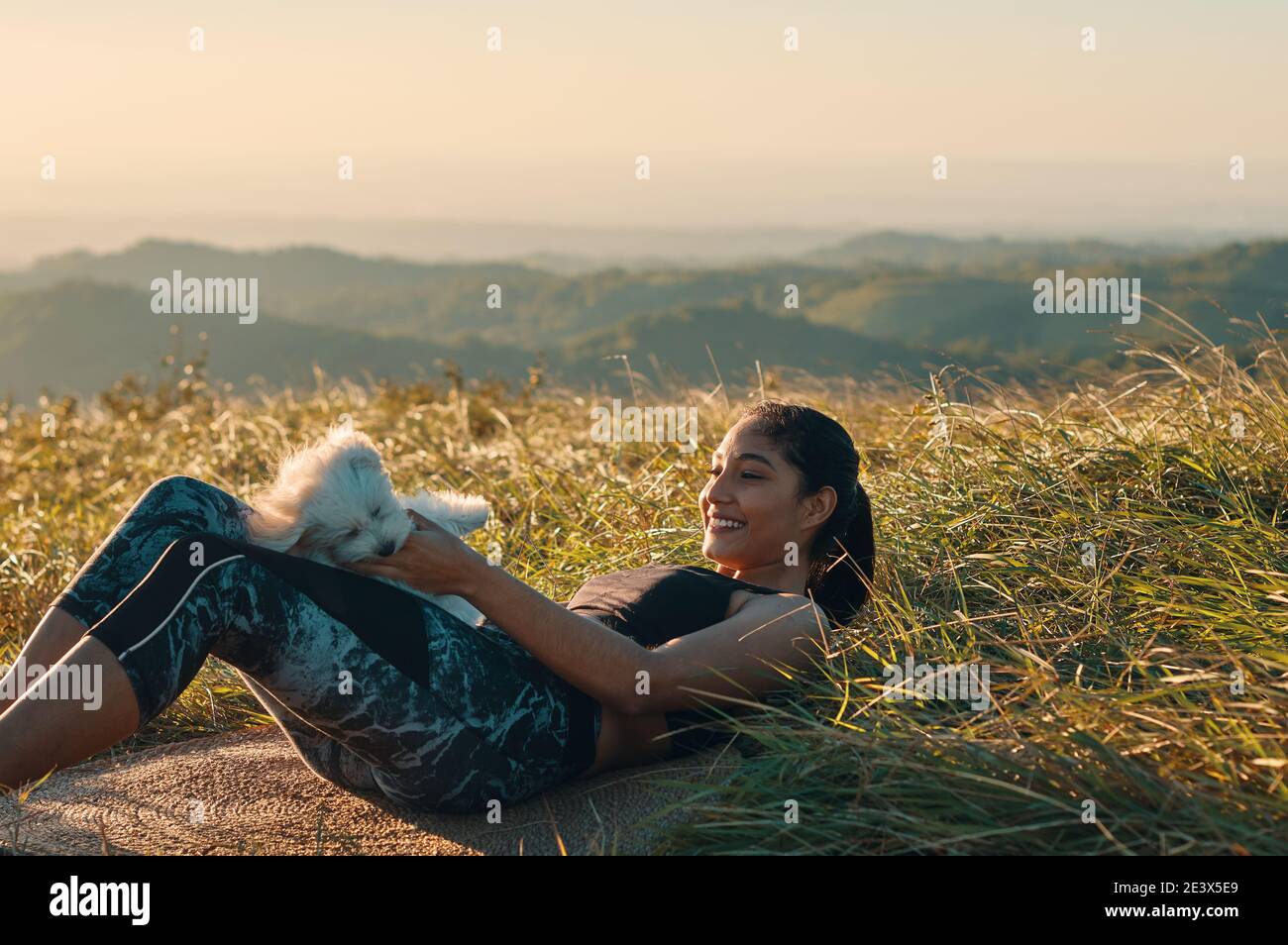 Eine Frau, die auf dem Gras liegt und mit ihr spielt Welpe Hund nach dem Training Stockfoto