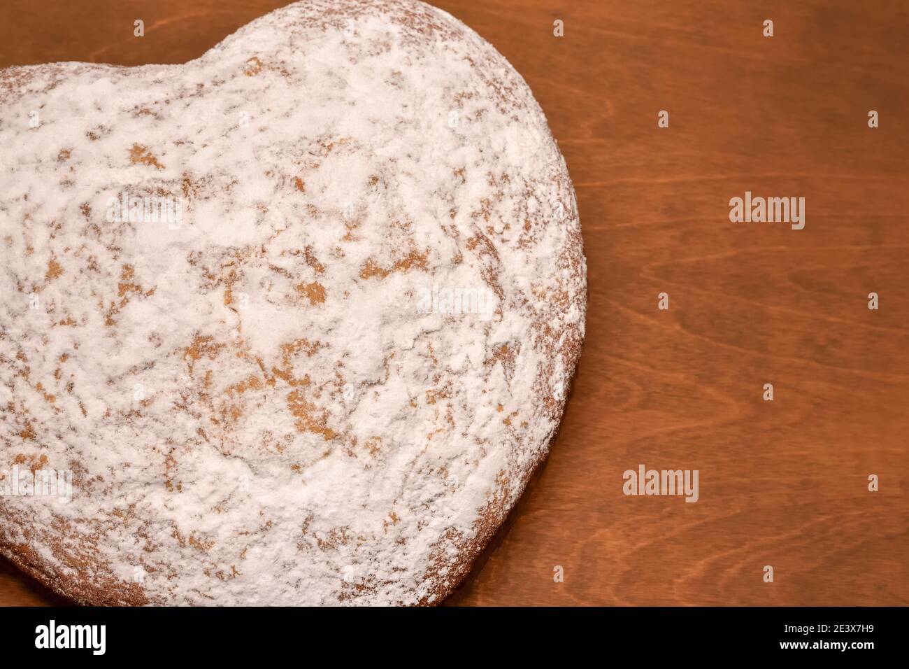 Herzförmiger Kuchen, frisch gebacken und mit Puderzucker bestäubt, Blick von oben auf einem Holztisch Hintergrund Stockfoto