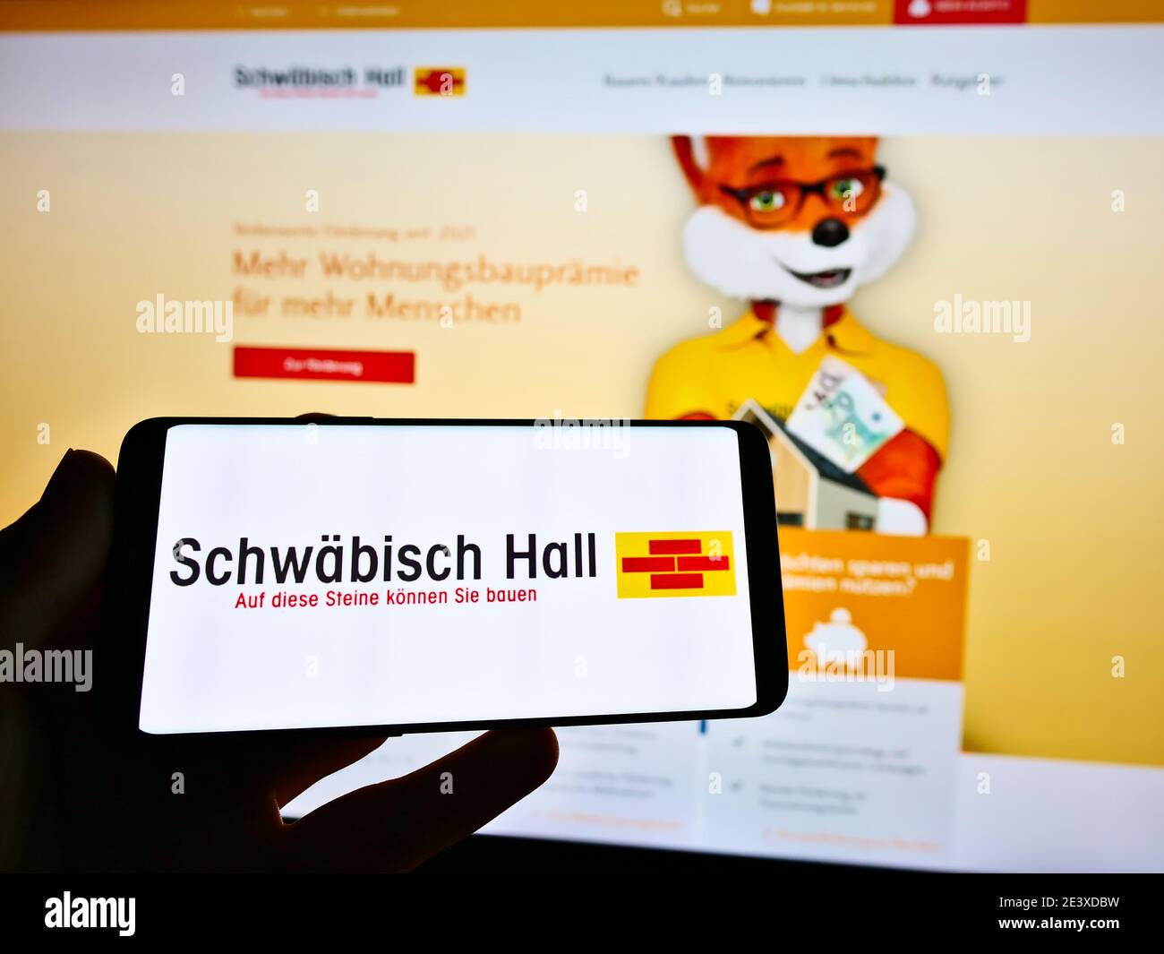 Person, die Smartphone mit Logo der Bausparkasse Schwäbisch Hall auf dem Bildschirm hält. Fokus auf der Mitte des Handy-Displays. Stockfoto