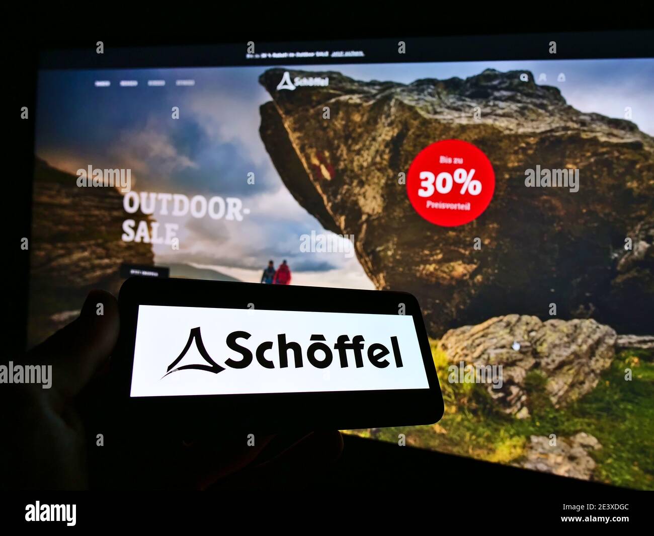 Person, die Smartphone mit Logo des Outdoor-Bekleidungsunternehmens Schöffel auf dem Bildschirm vor der Online-Shop-Website hält. Konzentrieren Sie sich auf den Mobiltelefon-Monitor. Stockfoto