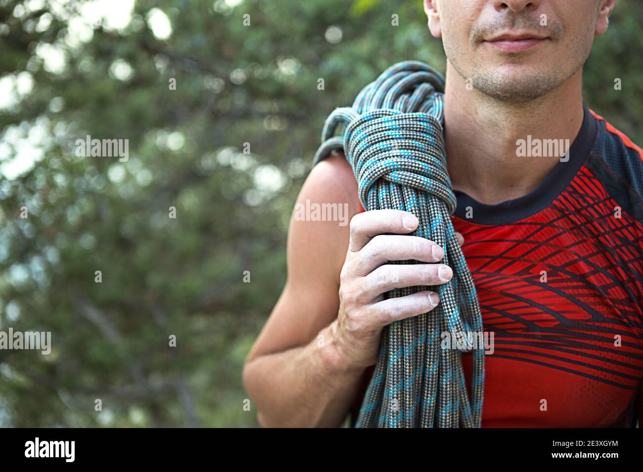 Ein männlicher Kletterer von kaukasischem Aussehen mit einem gewickelten Seil auf seiner Schulter. Hand in weißer Magnesia. Red Sports Trikot, Extremsport, Klettern. S Stockfoto