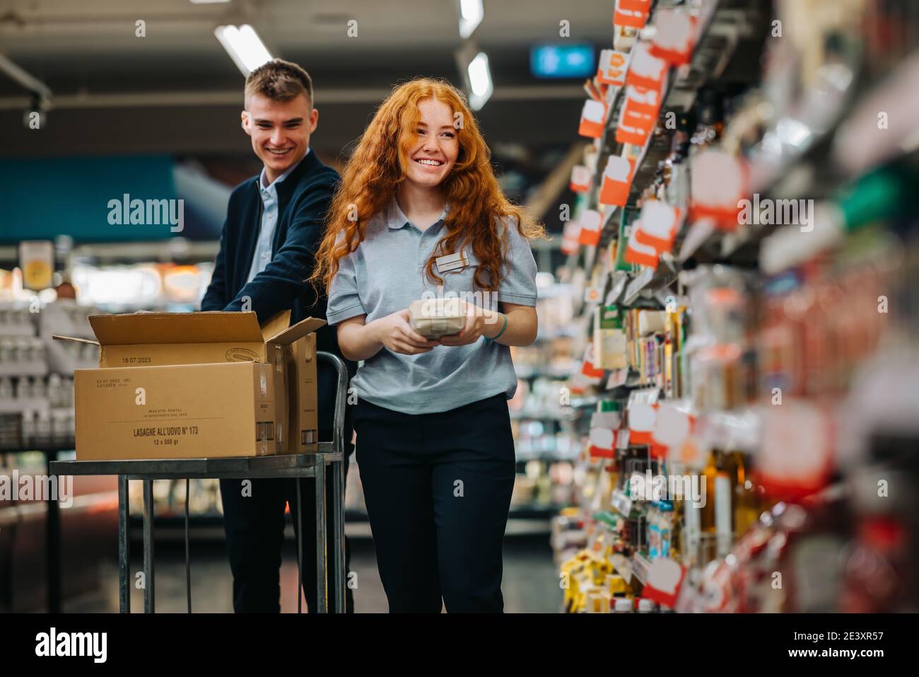 Zwei junge Arbeiter, die in einem Supermarkt arbeiten. Mann und Frau Supermarktmitarbeiter bei der Arbeit, die die Produktregale aufstocken. Stockfoto
