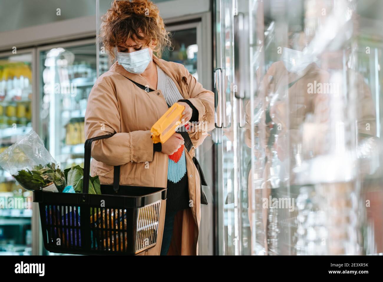 Frau mit Gesichtsmask, die Lebensmittel im Supermarkt kauft. Weibliche Kundin trägt Schutzgesichtsbemask Einkaufen im Supermarkt. Stockfoto