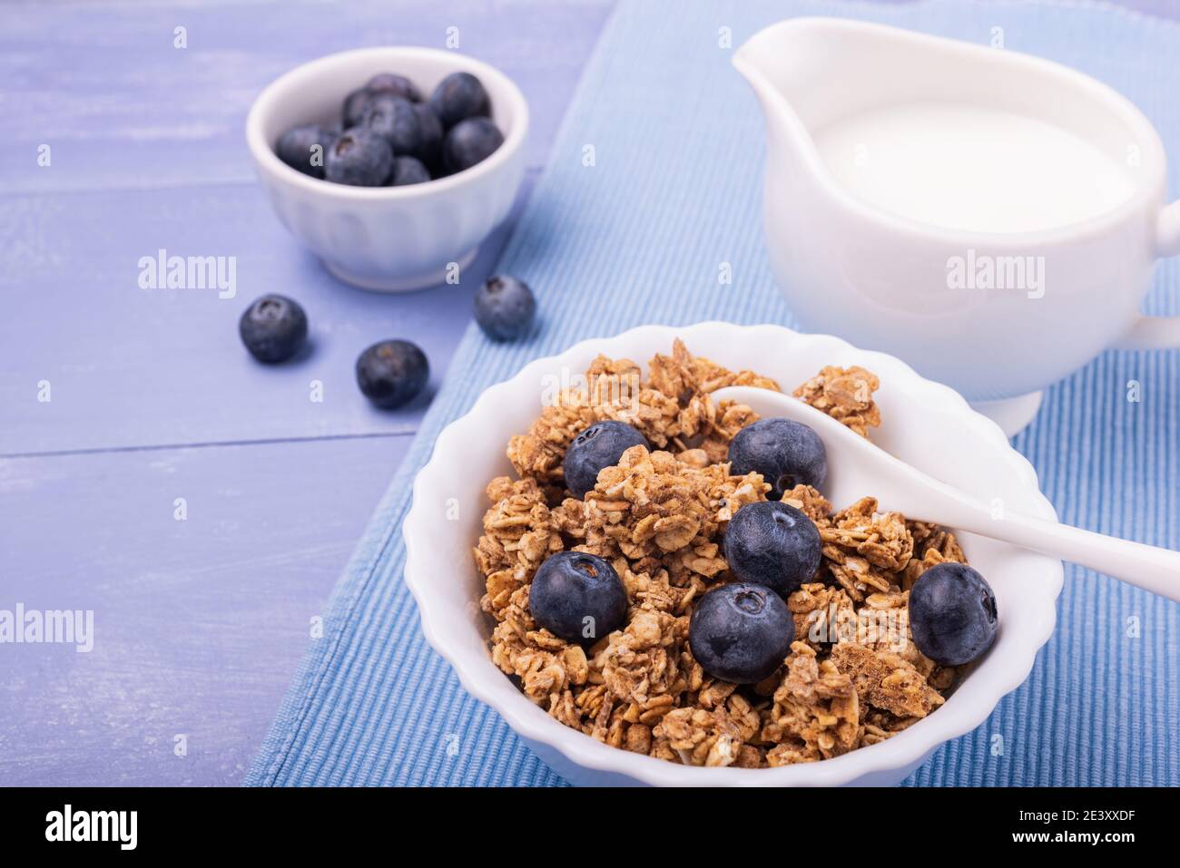 Auf dem Lavendelblauen Tisch, gesundes Frühstück mit knusprigen Vollkornmüsli aus Gerste und Hafer, Heidelbeeren und frischer Milch. Stockfoto