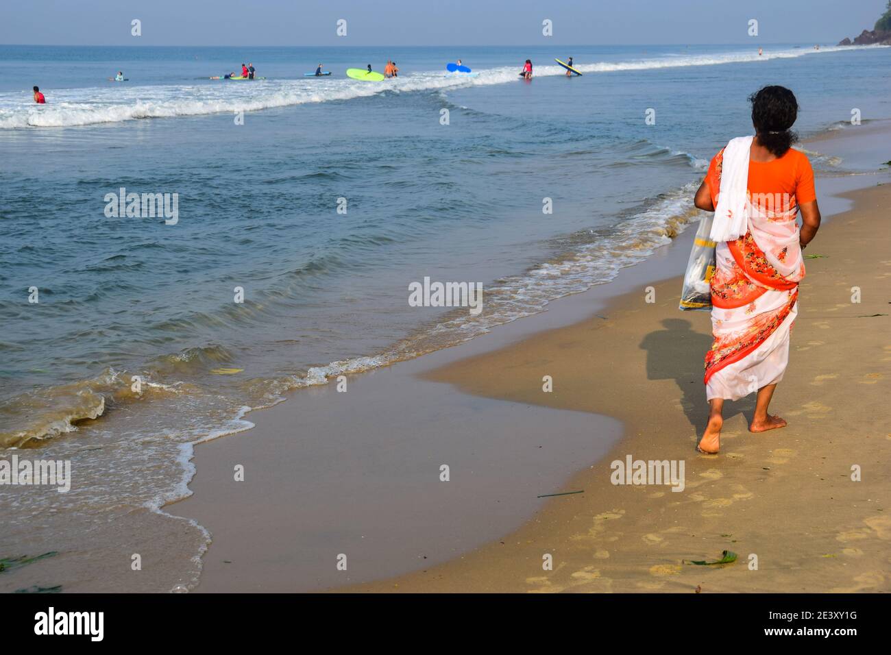 Kulturelle Gegenüberstellung, Surfers, Indian Lady in Sari Spaziergang am Varkala Beach, Varkala, Kerala, Indien Stockfoto