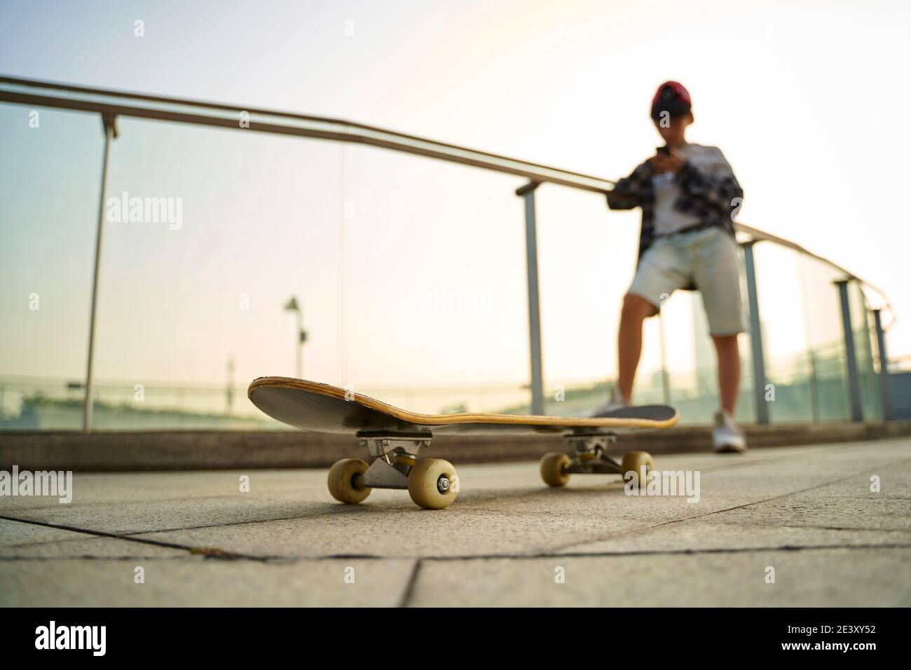 Teenage asiatische Skateboarder Junge Blick auf Handy während der Ruhe, konzentrieren Sie sich auf das Skateboard Stockfoto