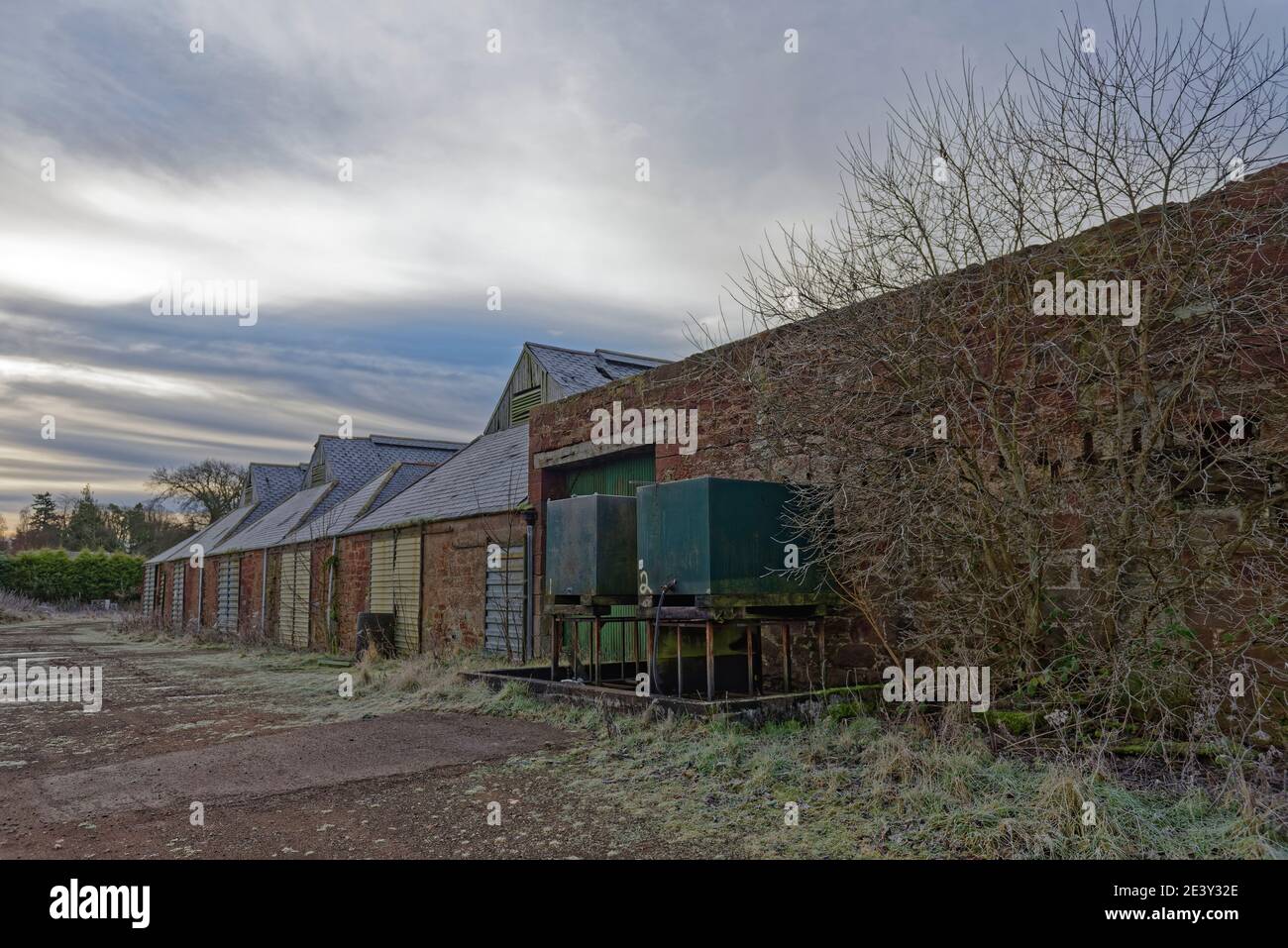 Ein ruiniertes Farmgebäude oder Landwirtschaftsladen mit zwei leeren Treibstofftanks neben einer der Steinmauern neben einer Metallschiebetür. Stockfoto