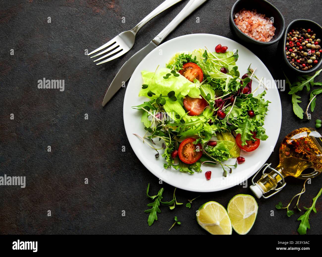 Frische grüne gemischte Salatschüssel mit Tomaten und Microgreens auf schwarzem Beton Hintergrund. Gesunde Ernährung, Draufsicht. Stockfoto