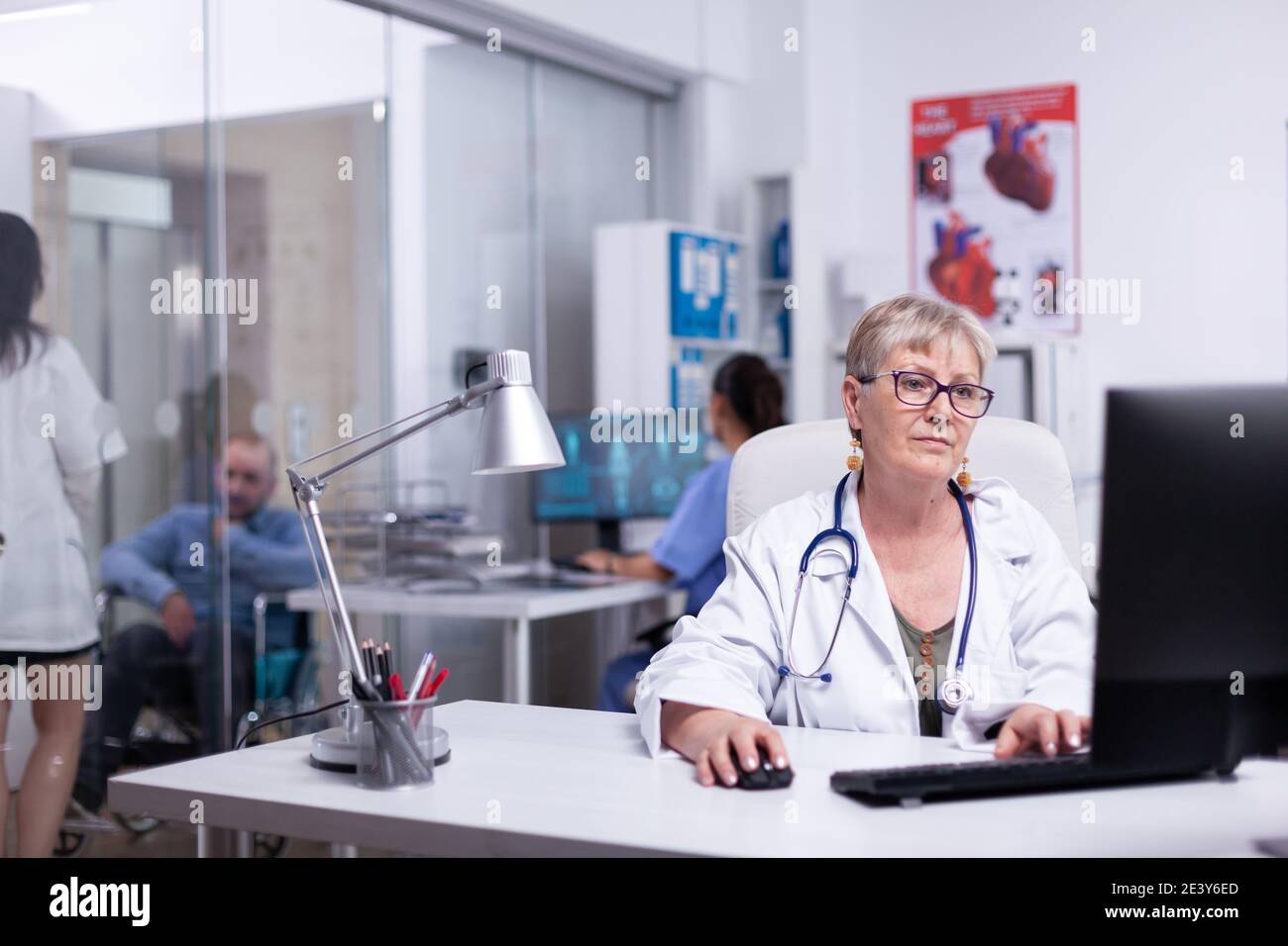 Team von Ärzten in der Klinik arbeiten, tippen am Computer, Krankenschwester Analyse Körper-Scan, während junge Sanitäter diskutieren mit behinderten verrückt im Warteraum. Fachkundiger Arzt, der am pc arbeitet und Daten eingibt Stockfoto