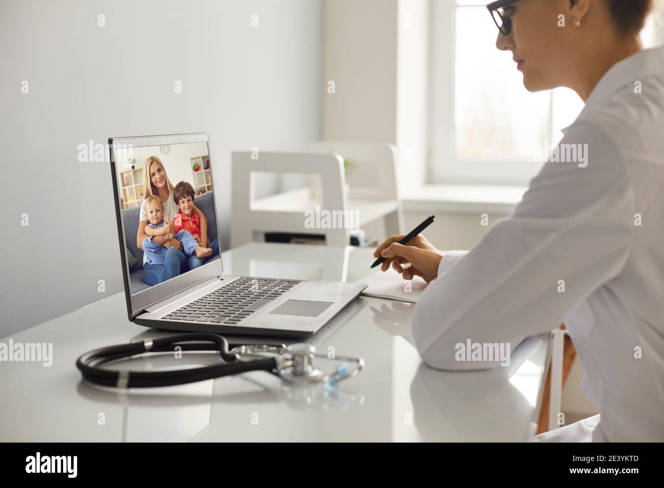Ärztin Notizen während Online-Beratung mit Frau und Zwei Kinder Stockfoto