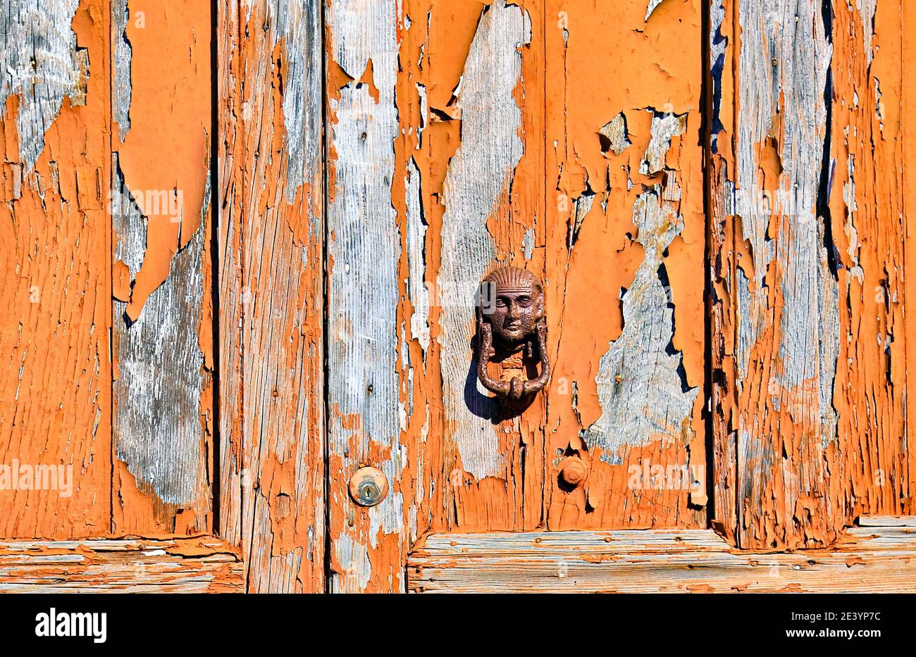 Der antike Türklopfer und die alte Holztür mit der abgeplatteten Farbe passen perfekt zusammen. Stockfoto