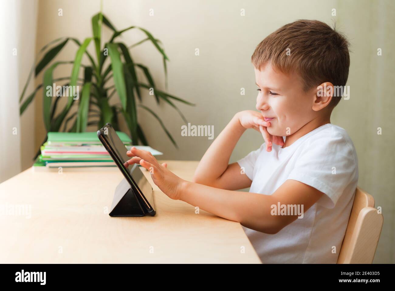 Nette Schuljunge macht Hausaufgaben mit Tablet am Schreibtisch. Kind, das Gadgets zum Lernen und Spielen verwendet. Homeschooling während der Quarantäne Stockfoto