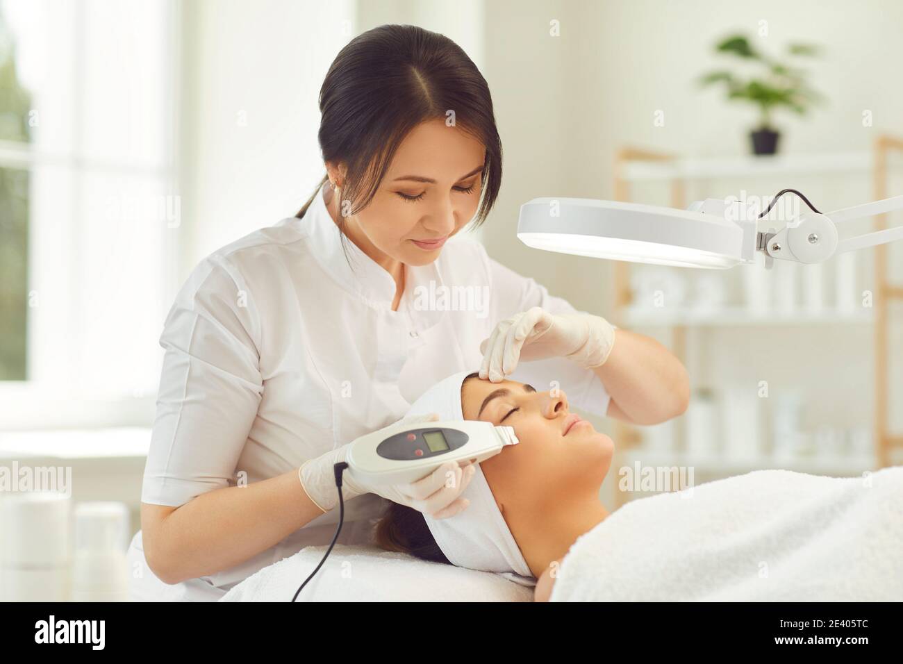 Lächelnder Dermatologe macht Ultraschall-Gerät Gesichtsreinigung für junge Frau Stockfoto