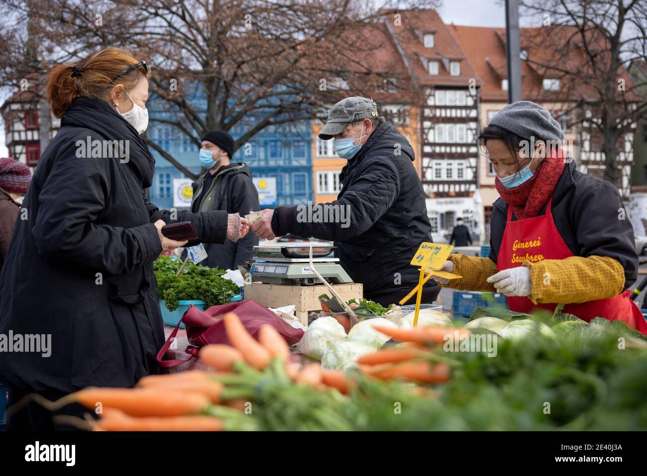 Erfurt, Deutschland. Januar 2021. Gemüsehändler aus der Gärtnerei Sauerbrey Erfurt verkaufen ihre Waren auf dem Domplatz mit Mundschutz. Im Stadtzentrum von Erfurt besteht die Pflicht, eine Mundnasenabdeckung zu tragen, wenn der Mindestabstand von 1.5 Metern nicht eingehalten werden kann. Quelle: Michael Reichel/dpa/Alamy Live News Stockfoto