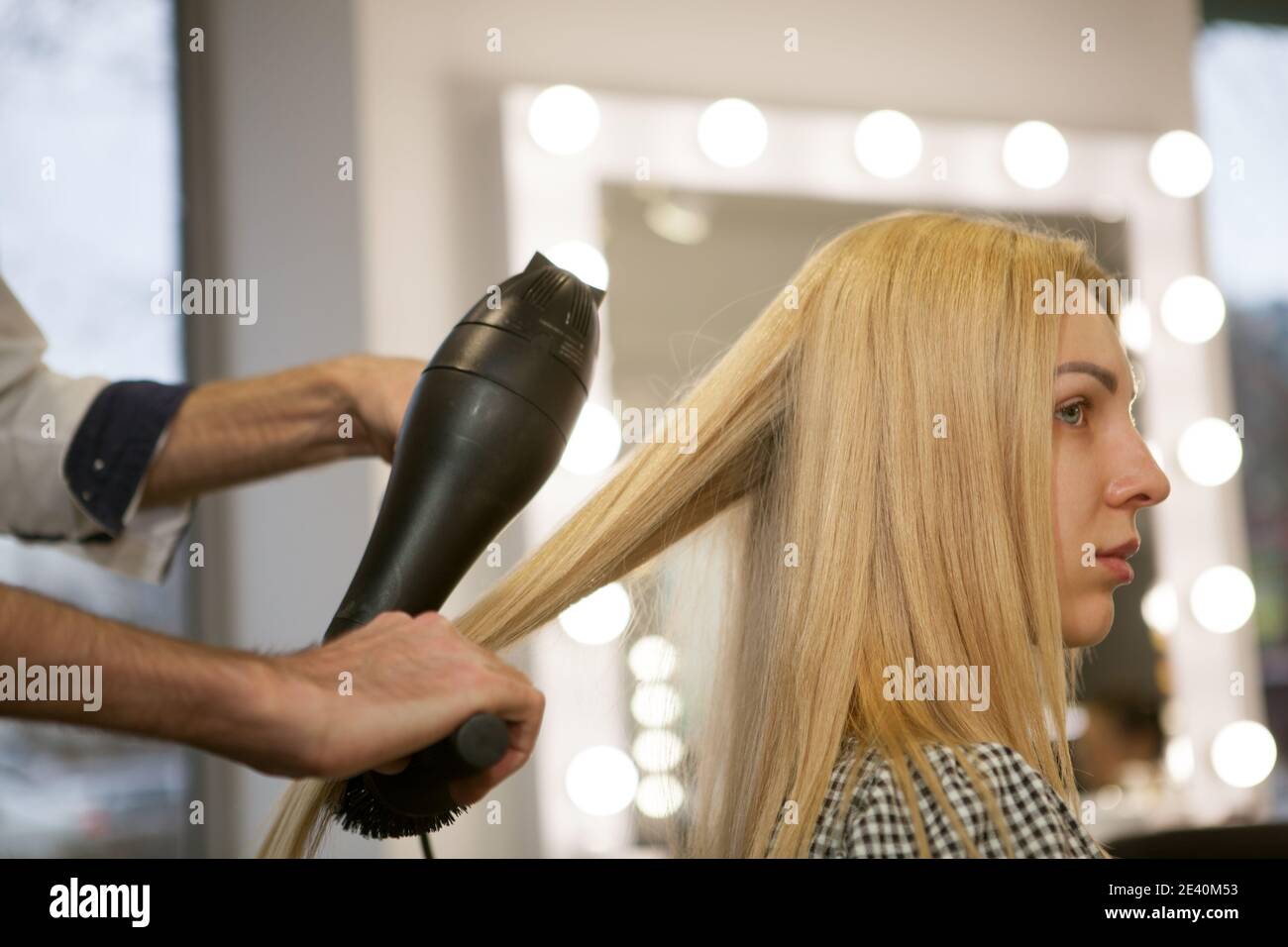 Kurzprofil-Aufnahme einer blonden haarigen Frau, die ihre Haare im Schönheitssalon stylen ließ. Professioneller Friseur mit Fön bei der Arbeit, Styling Haar Stockfoto