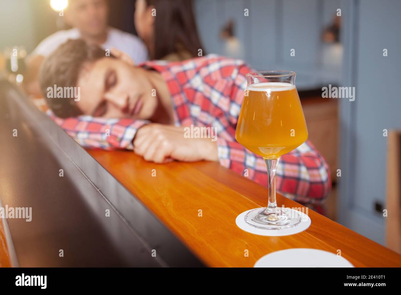 Selektive Konzentration auf ein Glas Bier an der Theke, junger Mann schläft betrunken in der Kneipe Stockfoto