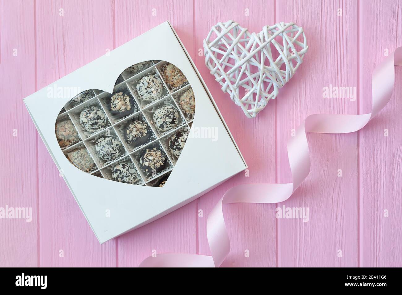 Schokolade handgemachte Bonbons auf rosa Holztisch. Schokoladenbox mit Herz und einem festlichen Band. Geschenk zum valentinstag Stockfoto