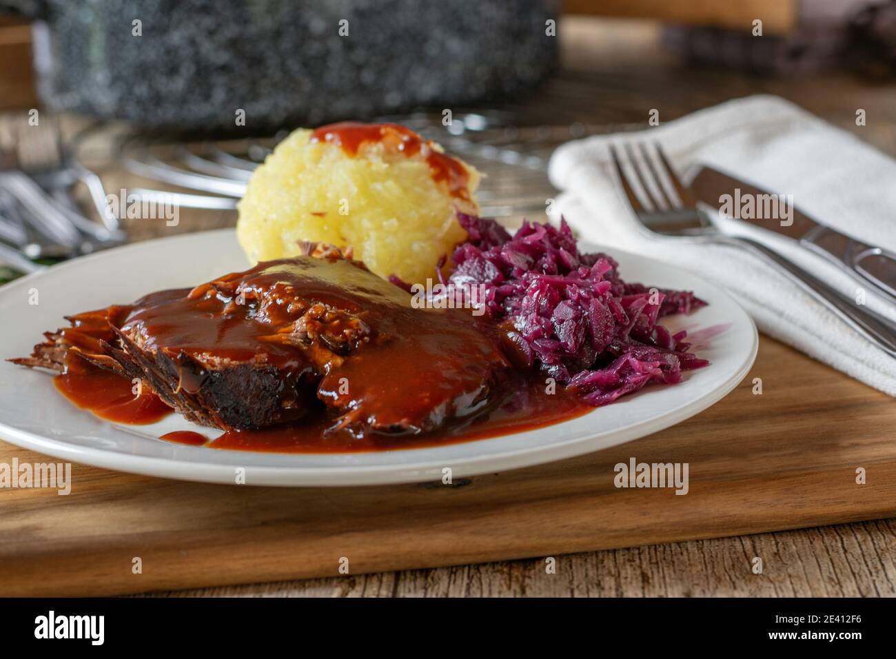 Ein Teller mit köstlichem Roastbeef mit Soße, Rotkohl und Kartoffeldumpling mit Messer und Gabel Stockfoto