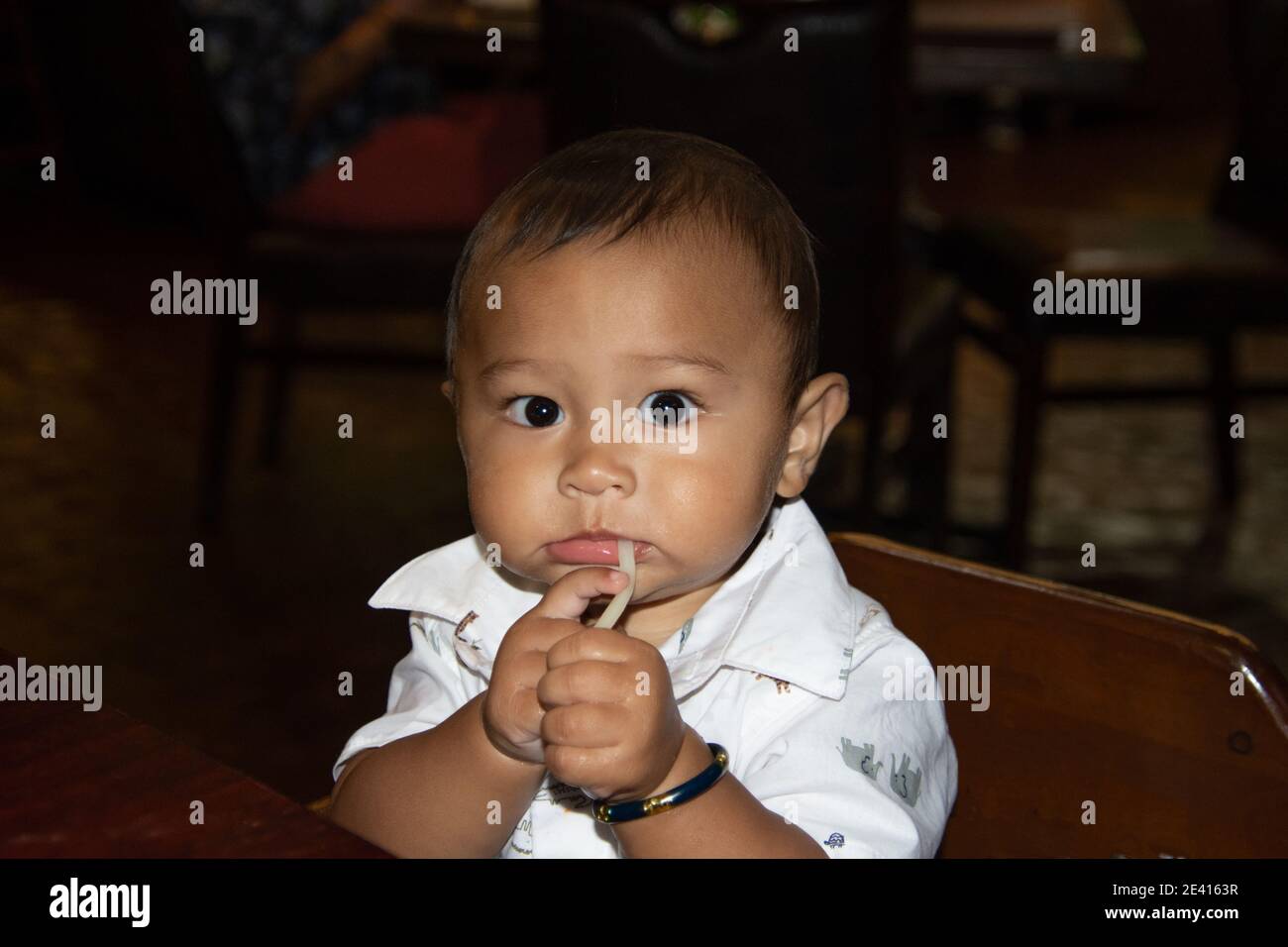 Filipino American Baby fasziniert von Udon Nudeln, wie er sitzt In seinem Hochstuhl breitäugig Stockfoto