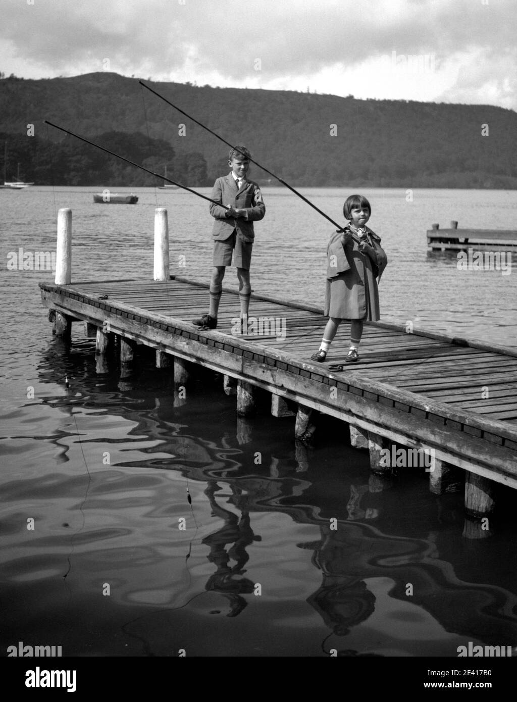 Ein Junge und ein Mädchen, möglicherweise Bruder und Schwester, fischen in einem See an einer Promenade, in den 1940er oder 1950er Jahren Stockfoto