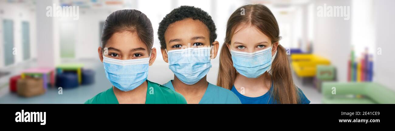 Multiethnische Gruppe von Kindern, die medizinische Masken tragen und in einem Schulflur stehen. Globale Pandemie, Quarantäne in der Schule Stockfoto