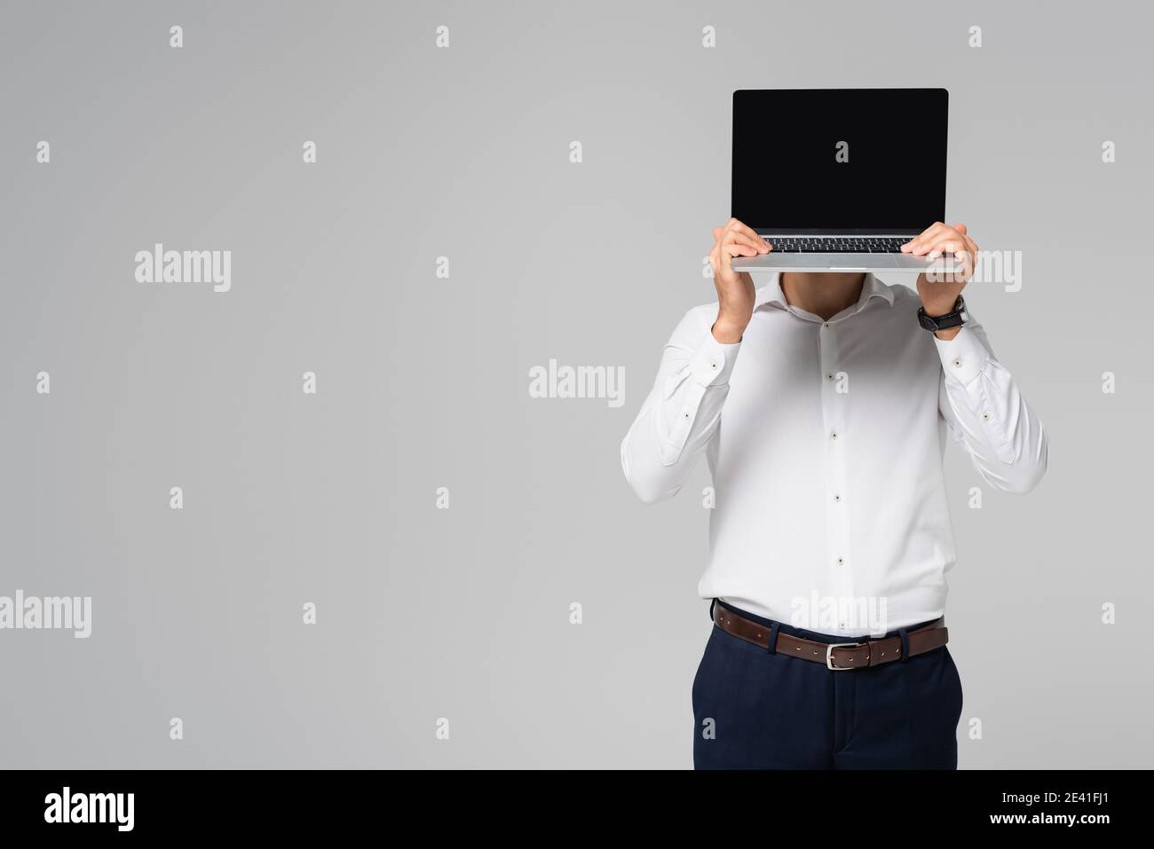 hispanic Geschäftsmann in weißem Hemd verdeckt Gesicht mit Laptop isoliert Auf Grau Stockfoto