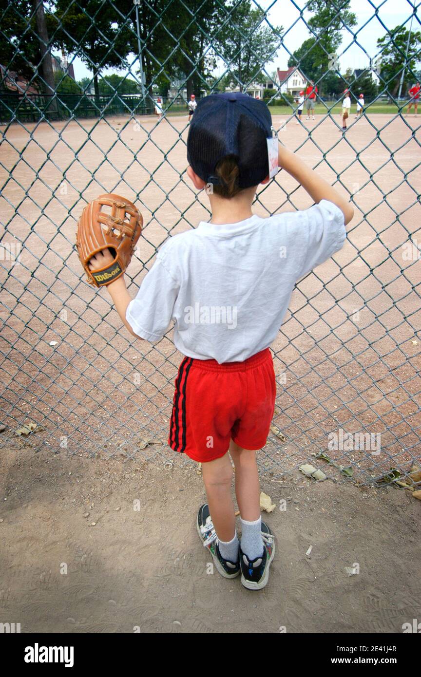 6 Jahre alt Junge Uhren Baseball T Ball Little League Aktion hinter einem Zaun Stockfoto