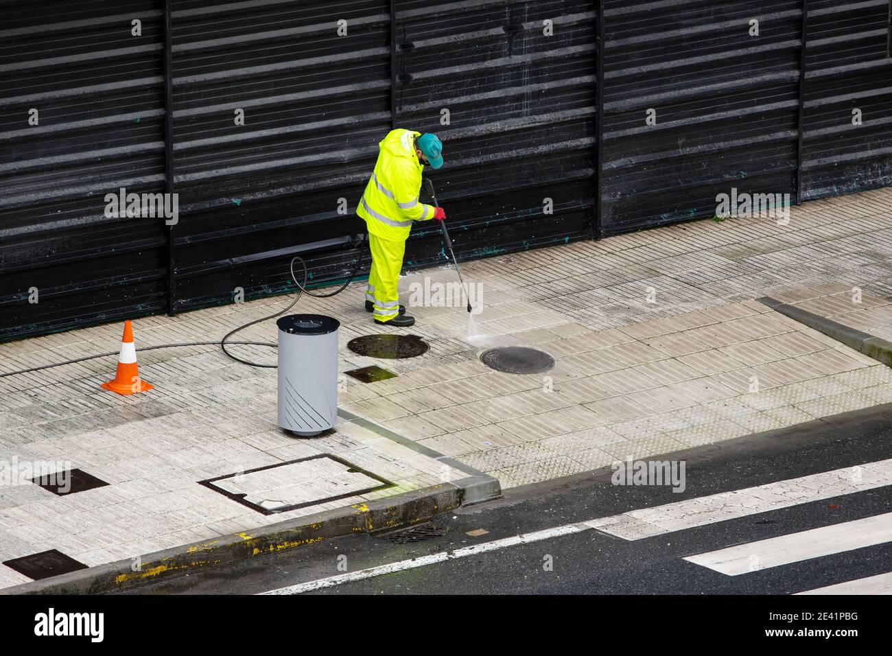 Kehrmaschine Arbeiter Reinigung einer Straße Bürgersteig mit Hochdruck-Wasserstrahlmaschine an regnerischen Tag. Speicherplatz kopieren Stockfoto