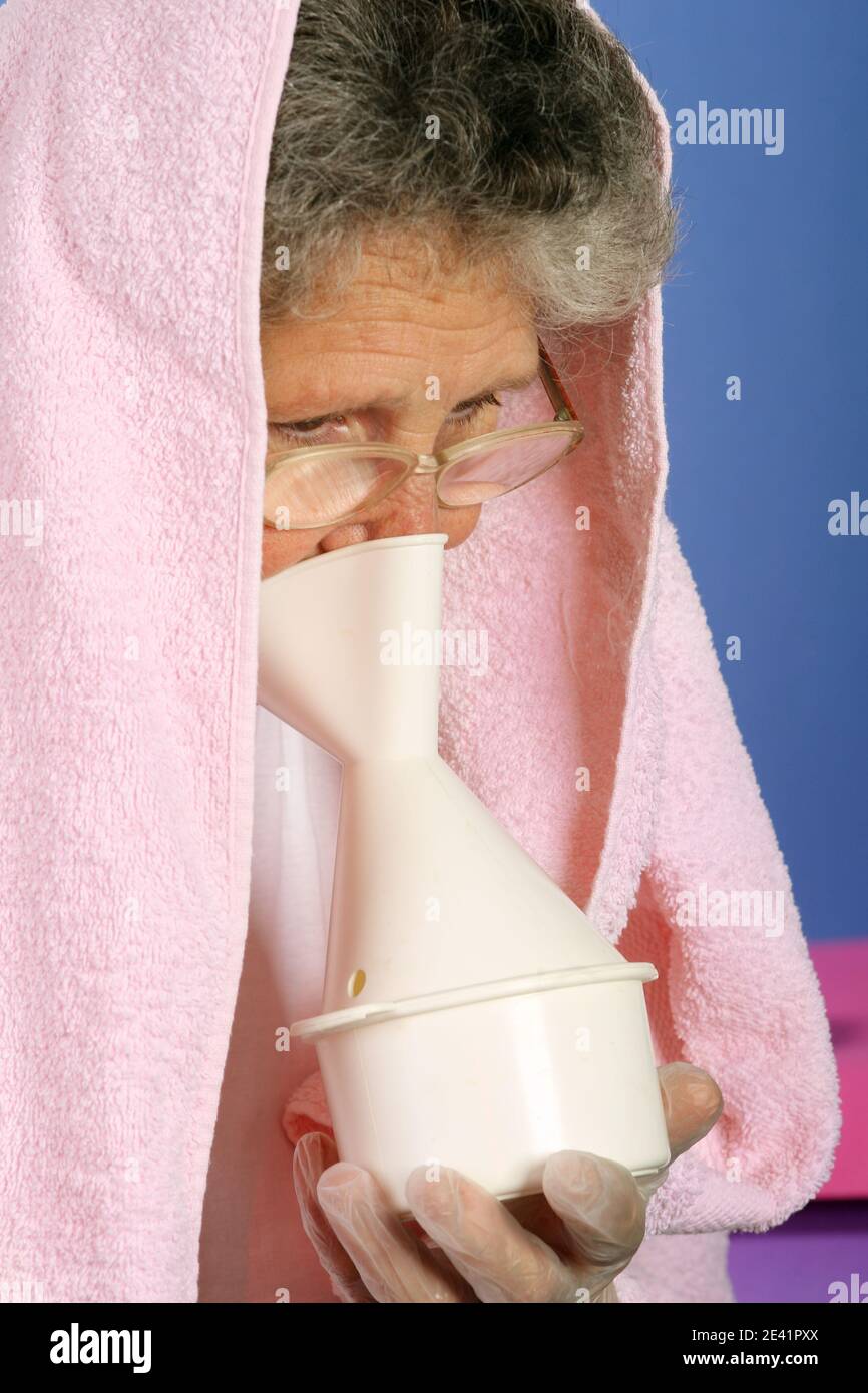65-jährige Frau mit Handtuch über Kopf inhalieren unerlässlich Öldampf als alternative Therapie Stockfoto