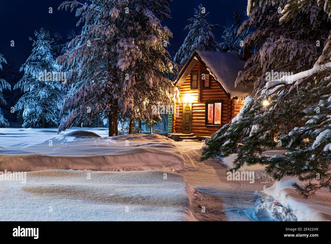 Rustikales Blockhaus, schneebedeckte Pinien, große Schneeverwehungen, fabelhafte Winternacht Stockfoto