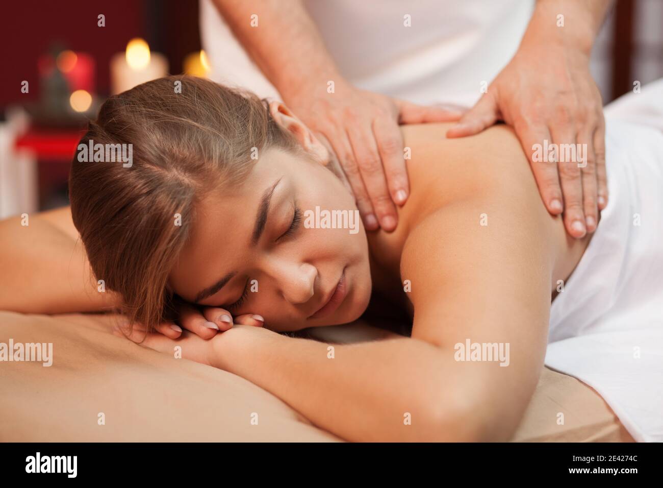 Entspannte junge Frau genießen beruhigende Massage in den Händen von erfahrenen Masseur. Spa-Therapeut arbeitet mit seiner Klientin zusammen und massiert ihren Rücken am Strand Stockfoto