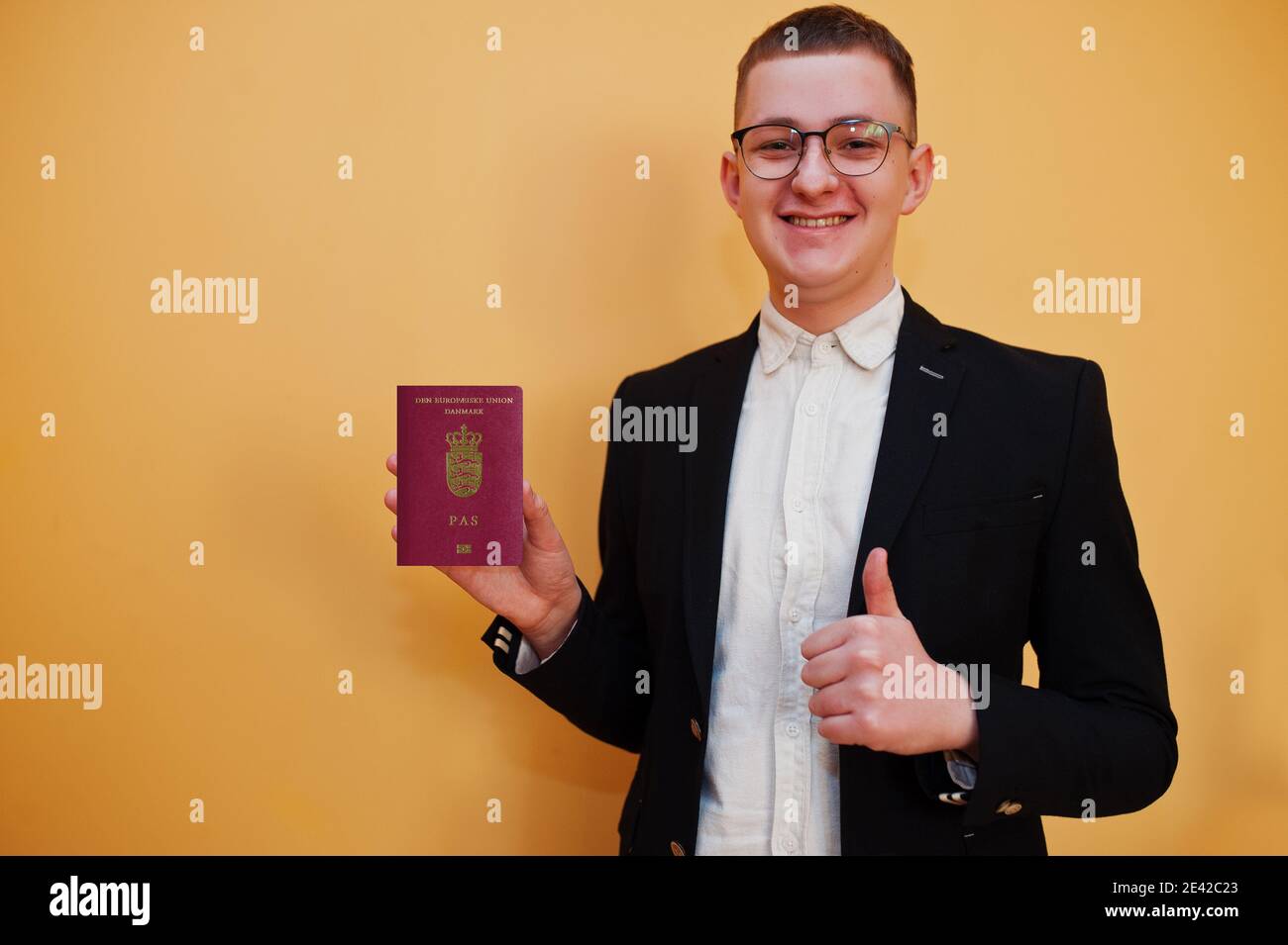 Junger schöner Mann hält Königreich Dänemark Pass-id über gelbem Hintergrund, glücklich und zeigen Daumen nach oben. Reise nach Europa Country Konzept. Stockfoto