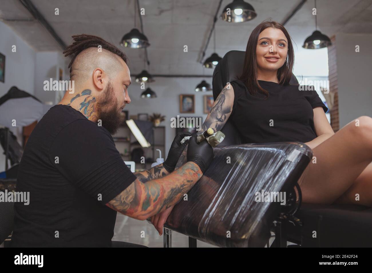 Low-Winkel-Aufnahme einer schönen jungen Frau bekommen Arm Ärmel Tattoo von professionellen Tätowierer. Tattoo-Künstler arbeitet in seinem Salon, tätowieren schöne FEM Stockfoto