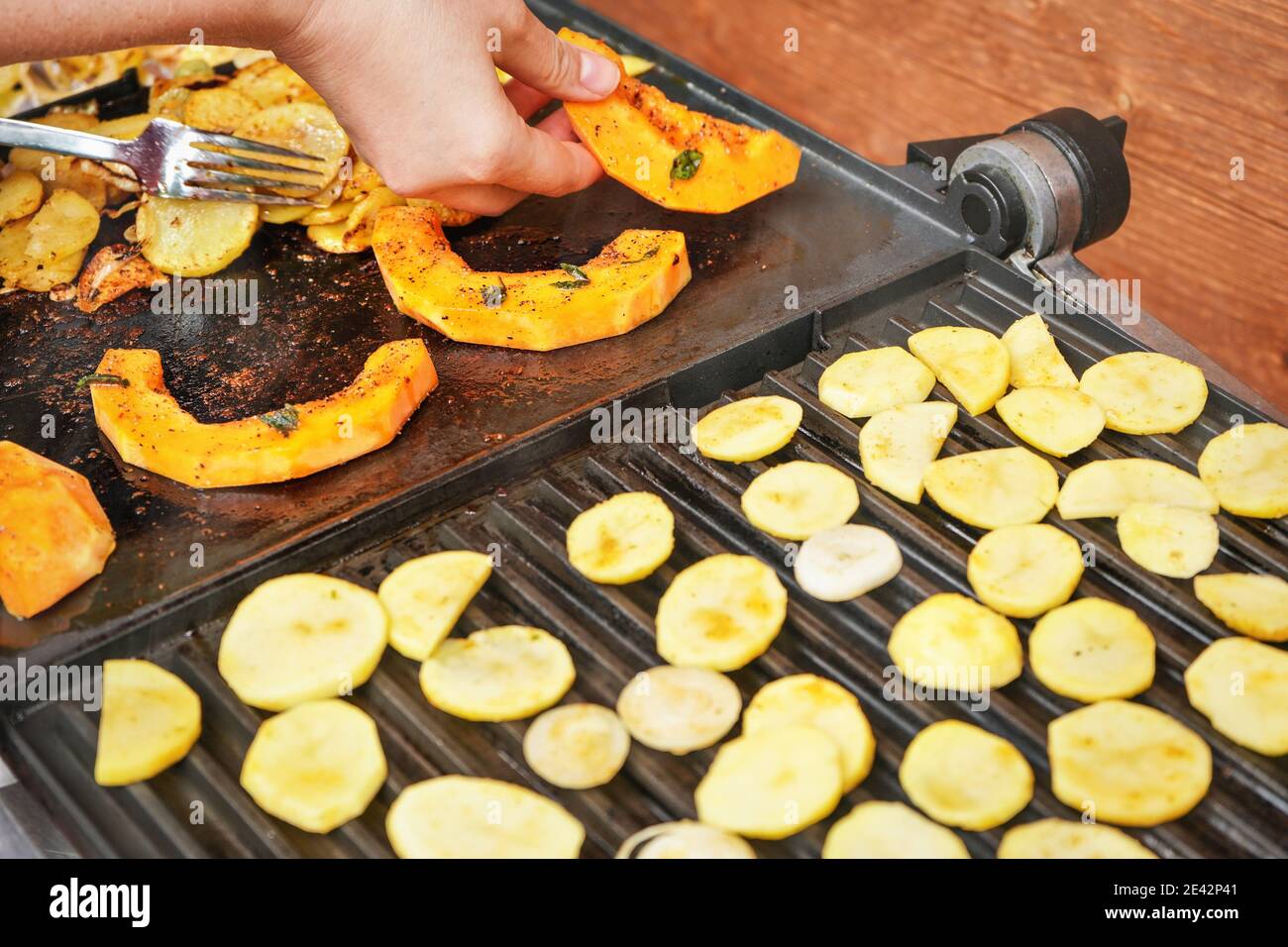 Leuchtend orange Butternut Squash Stücke auf elektrischen Grill gegrillt, Frau Hände bewegen Gemüse, verschwommen Kartoffelchips auch im Vordergrund gekocht Stockfoto