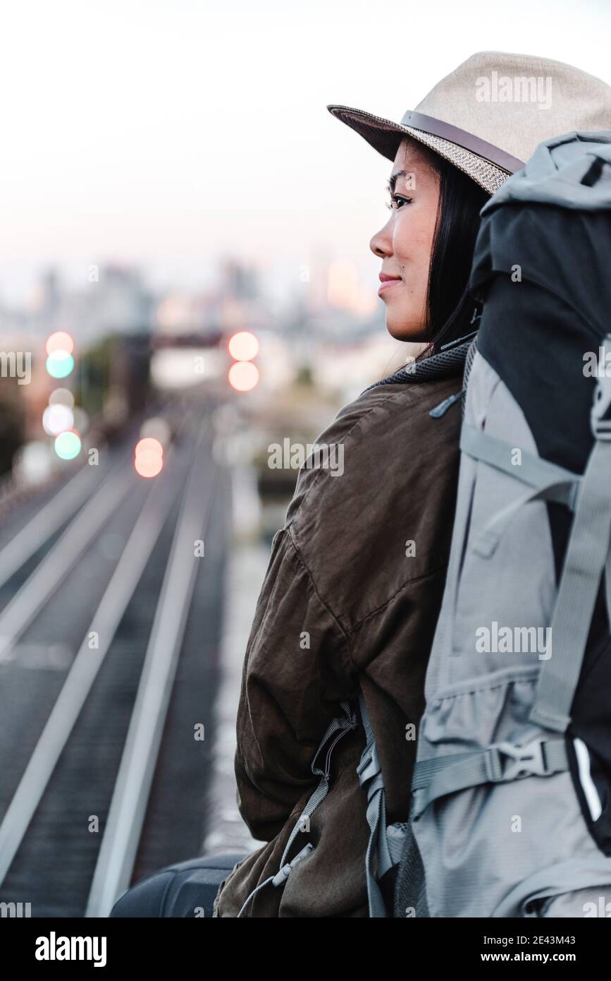 Rückansicht der erfreut asiatische weibliche Backpacker sitzt auf Hintergrund Der Eisenbahn und Blick weg über Schulter während des Abenteuers in Australien Stockfoto