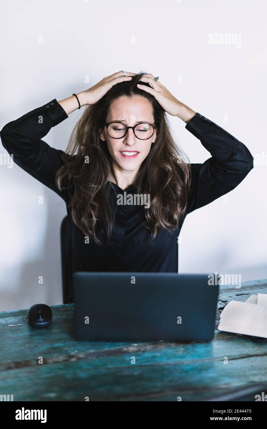 Frustriert junge weibliche Remote-Mitarbeiter in Brille berühren Kopf und Blick auf Laptop-Bildschirm, während immer Problem während der Telearbeit aus Heimbüro Stockfoto