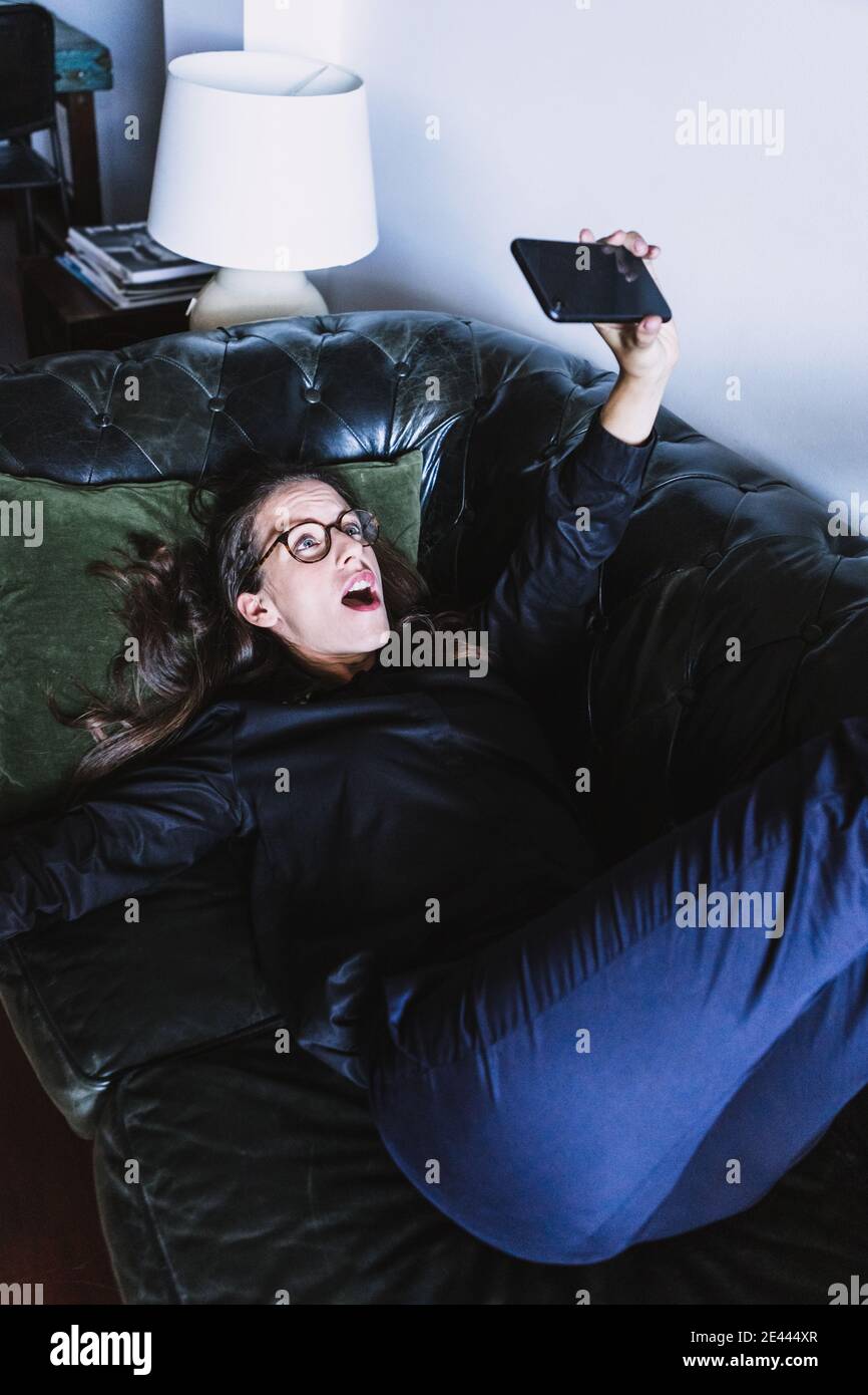 Oben der fröhlichen jungen Frau, die Spaß hat und nimmt Selfie auf dem Smartphone, während Sie sich zu Hause auf dem Sofa ausruhen Stockfoto