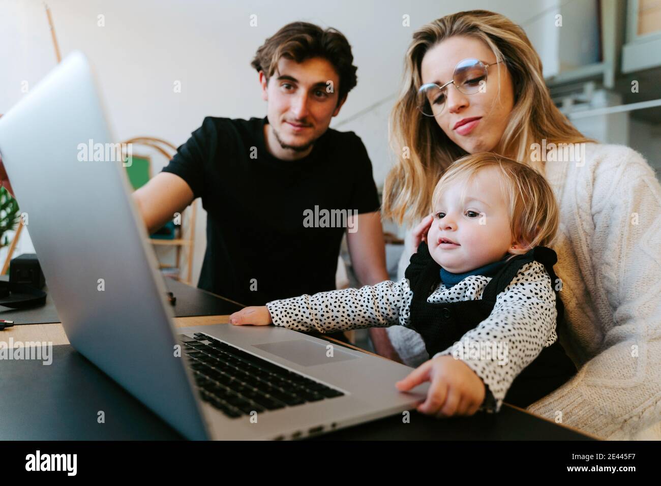 Junges Paar und Kleinkind sitzen am Tisch und schauen Film Zusammen, während Sie das Wochenende zu Hause verbringen Stockfoto