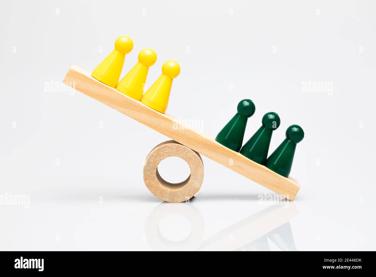 Grüne und gelbe Spielsteine auf einer hölzernen Wippe. Konzeptionelle Aufnahmen rund um Vergleich, Wettbewerb von Teams, gewinnende Gruppen und Differenzierung. Stockfoto