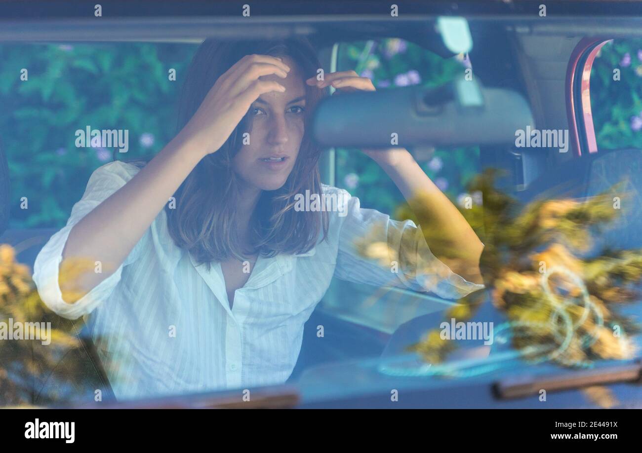 Durch die Windschutzscheibe der charmanten weiblichen Fahrer im Auto sitzen und Blick in den Rückspiegel, während die Anpassung der Haare Stockfoto